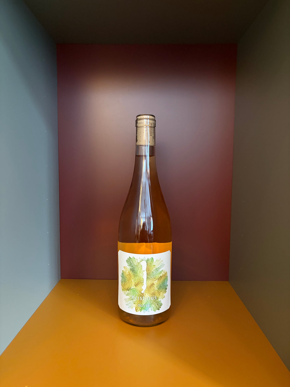 Wine bottle with pale gold liquid and white label with green leaf design