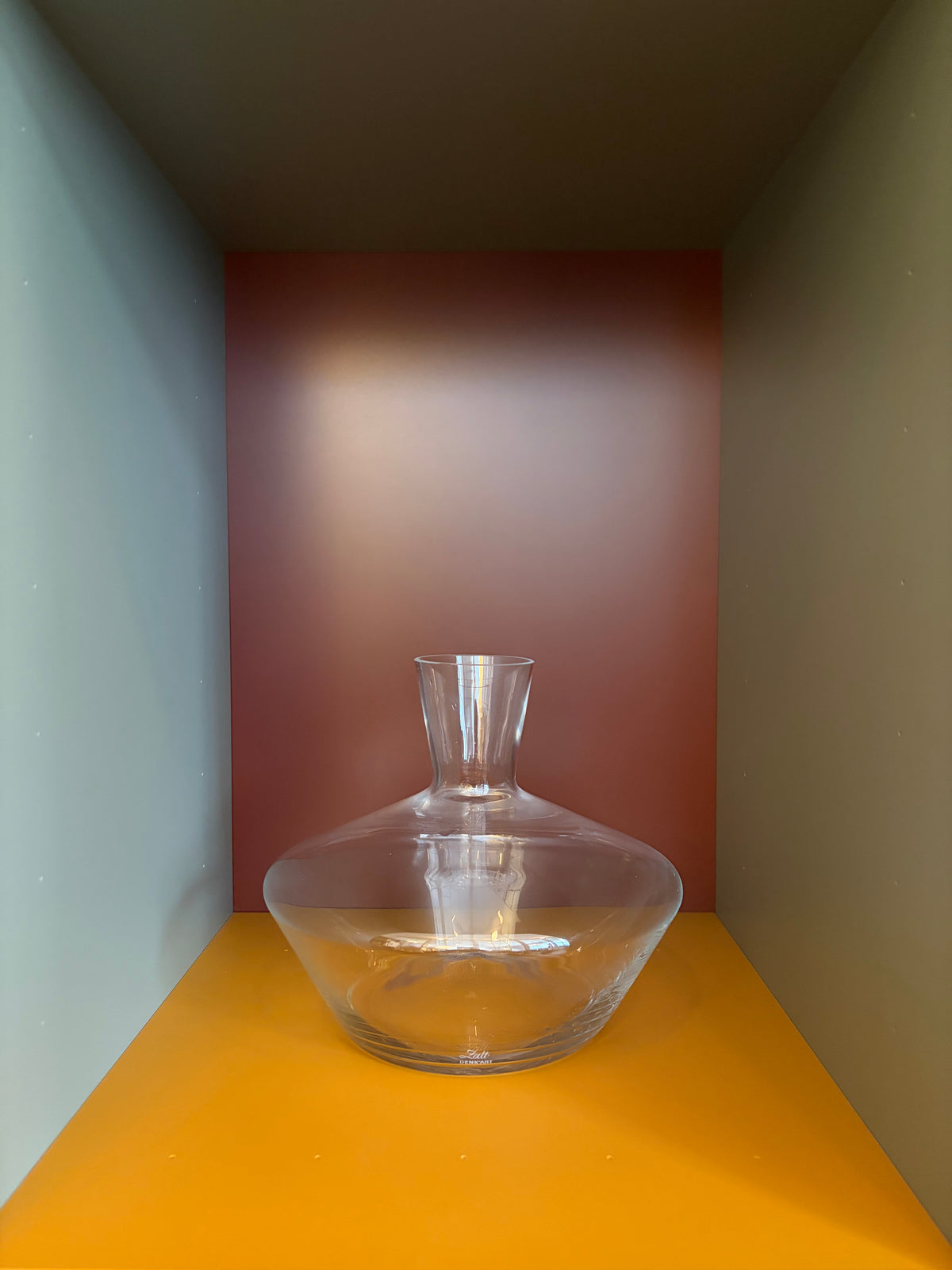 Clear glass decanter with wide base and narrow neck, partly filled with amber liquid